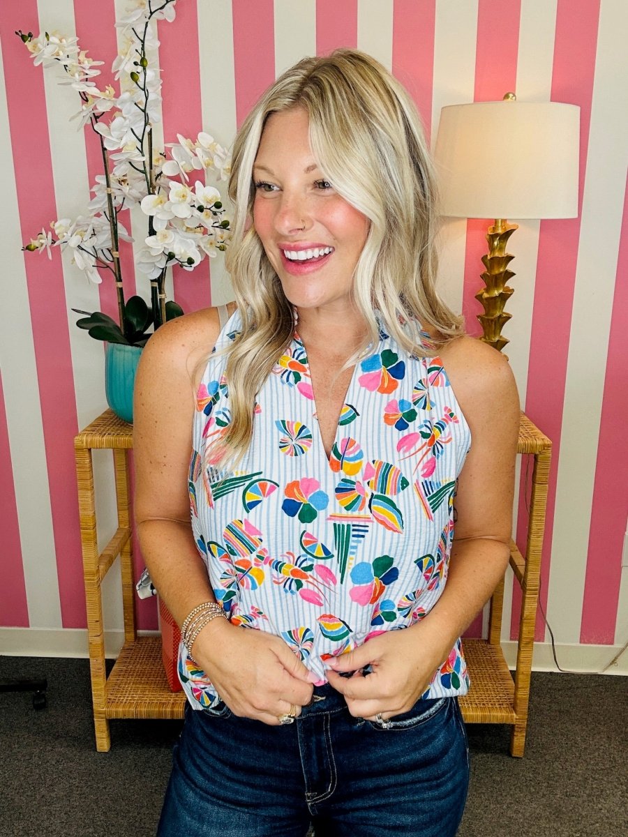 Woman wearing a colorful floral top in a room with striped walls and a lamp.