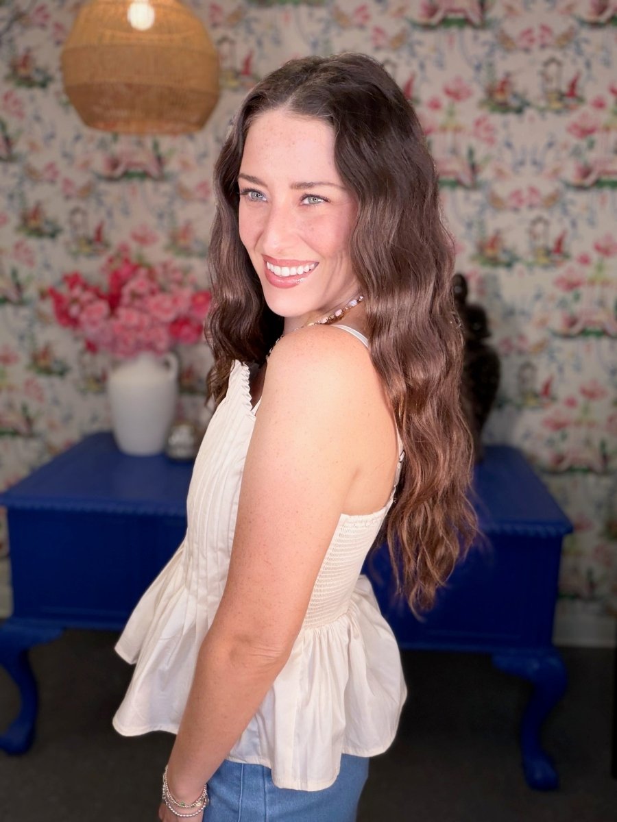 Woman in a white top and blue jeans standing in a room with floral wallpaper and a blue table.