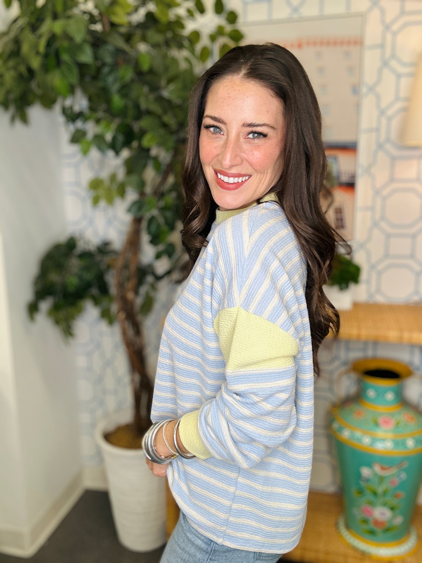Woman wearing a light blue and yellow striped sweater in a room with plants and decor.