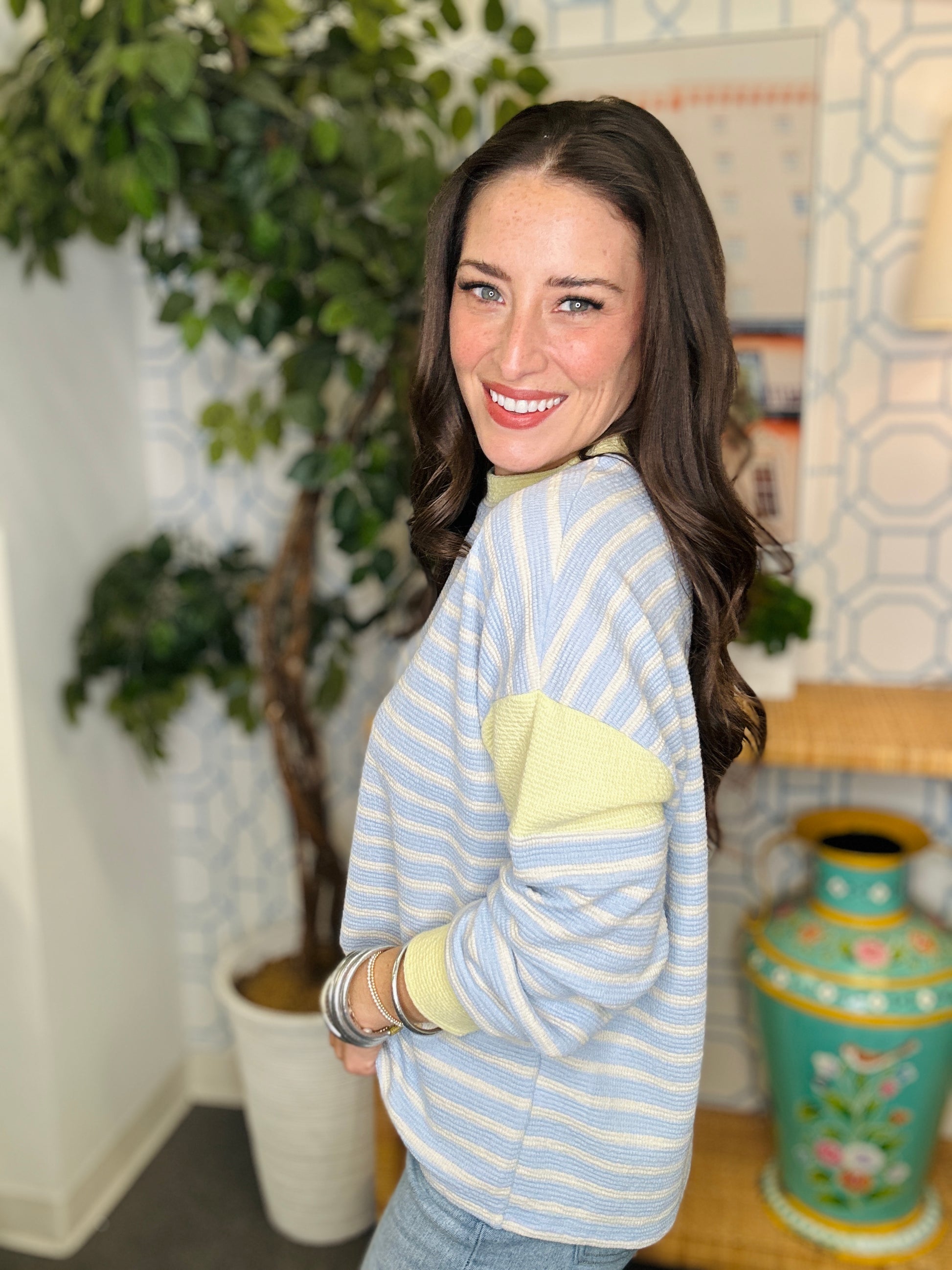 Woman wearing a light blue and yellow striped sweater in a room with plants and decor.