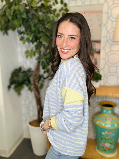 Woman wearing a light blue and yellow striped sweater in a room with plants and decor.