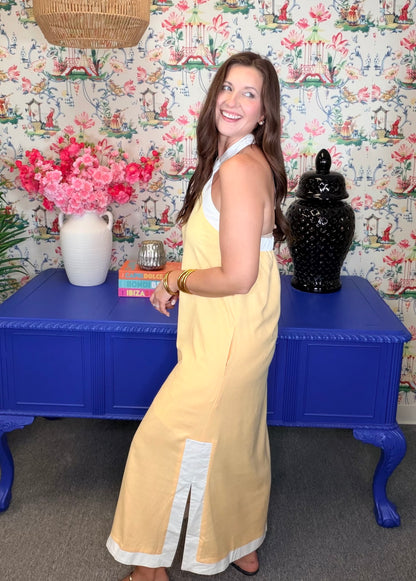Woman in a yellow dress standing in front of a colorful floral-patterned wall with a blue table and decorative items.
