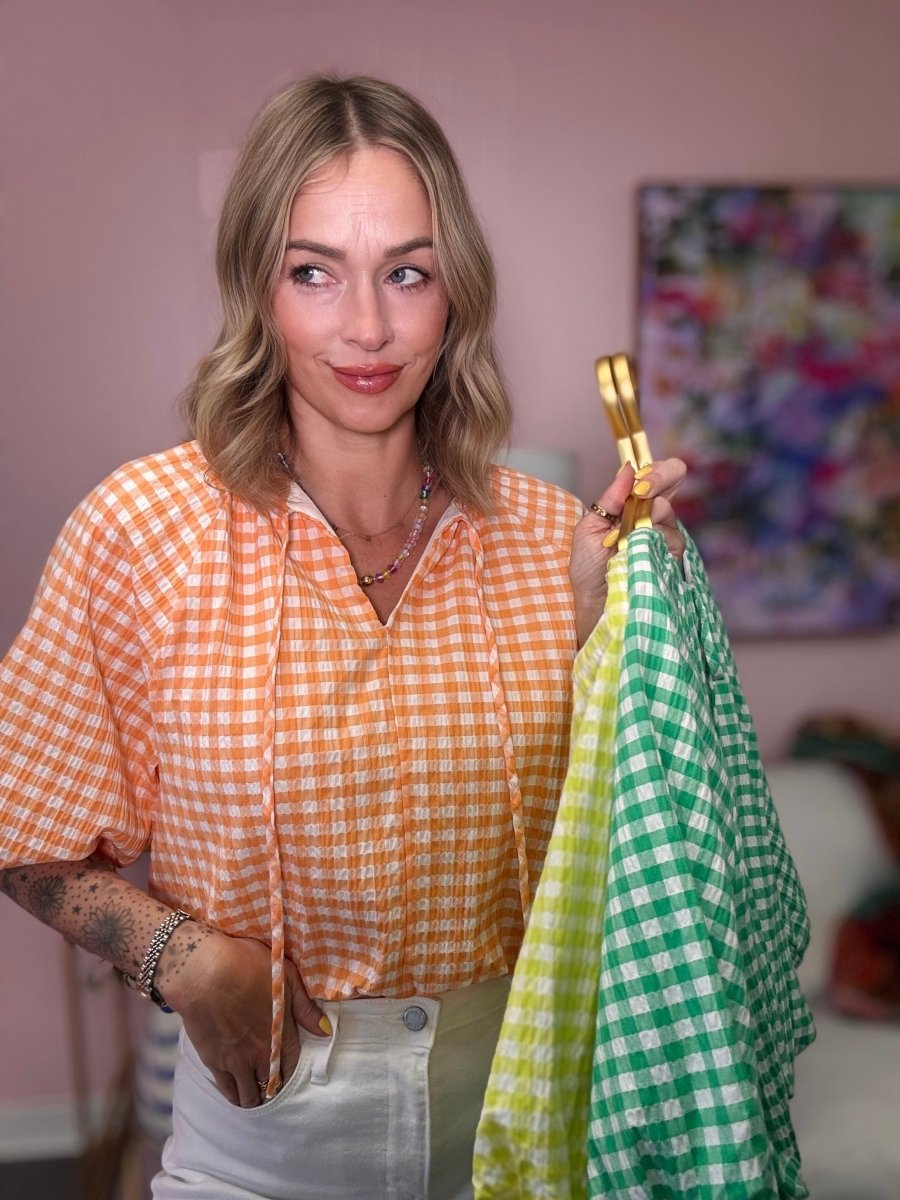 Woman holding two checkered cloths, one yellow and one green, in a room with a colorful painting on the wall.