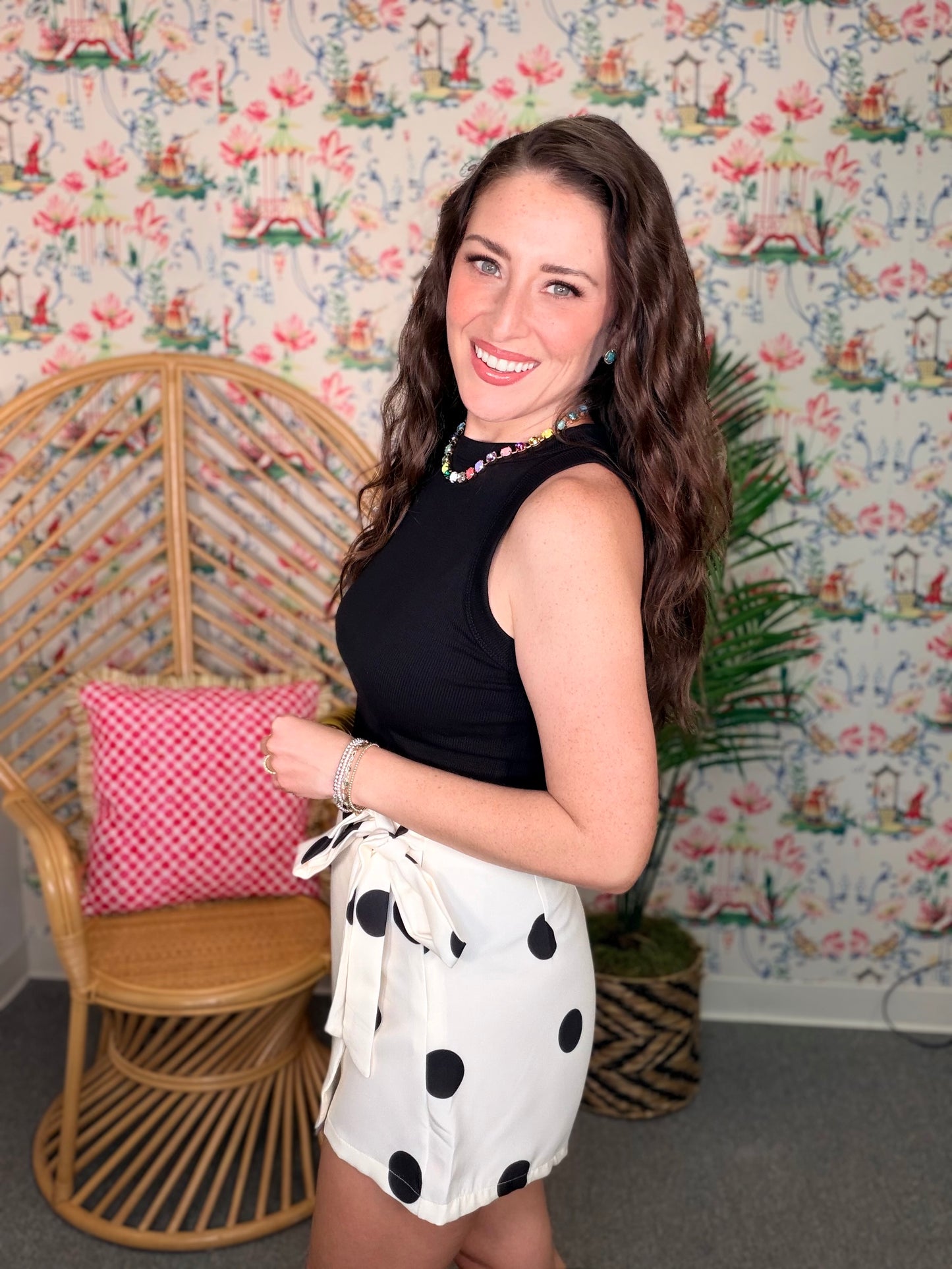 Woman in a black top and polka dot shorts standing in a room with floral wallpaper.