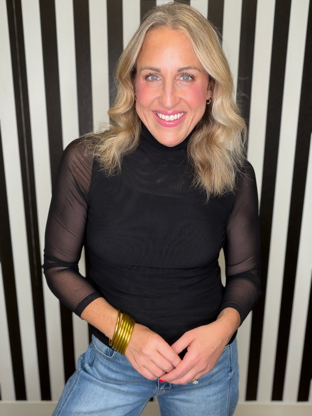 Woman in a black mesh top standing in front of a Black and white striped wall.