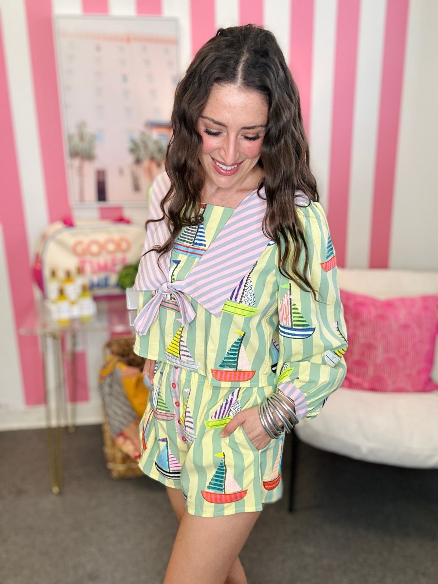 Woman wearing a colorful dress with a pattern of boats in a room with pink and white striped walls.