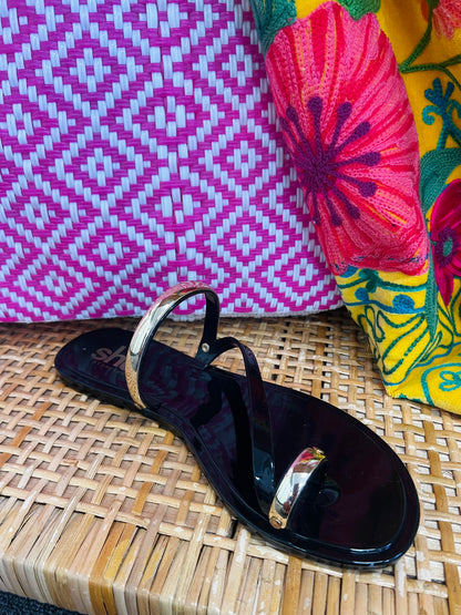 Black sandal with gold accents on a woven surface next to colorful fabric