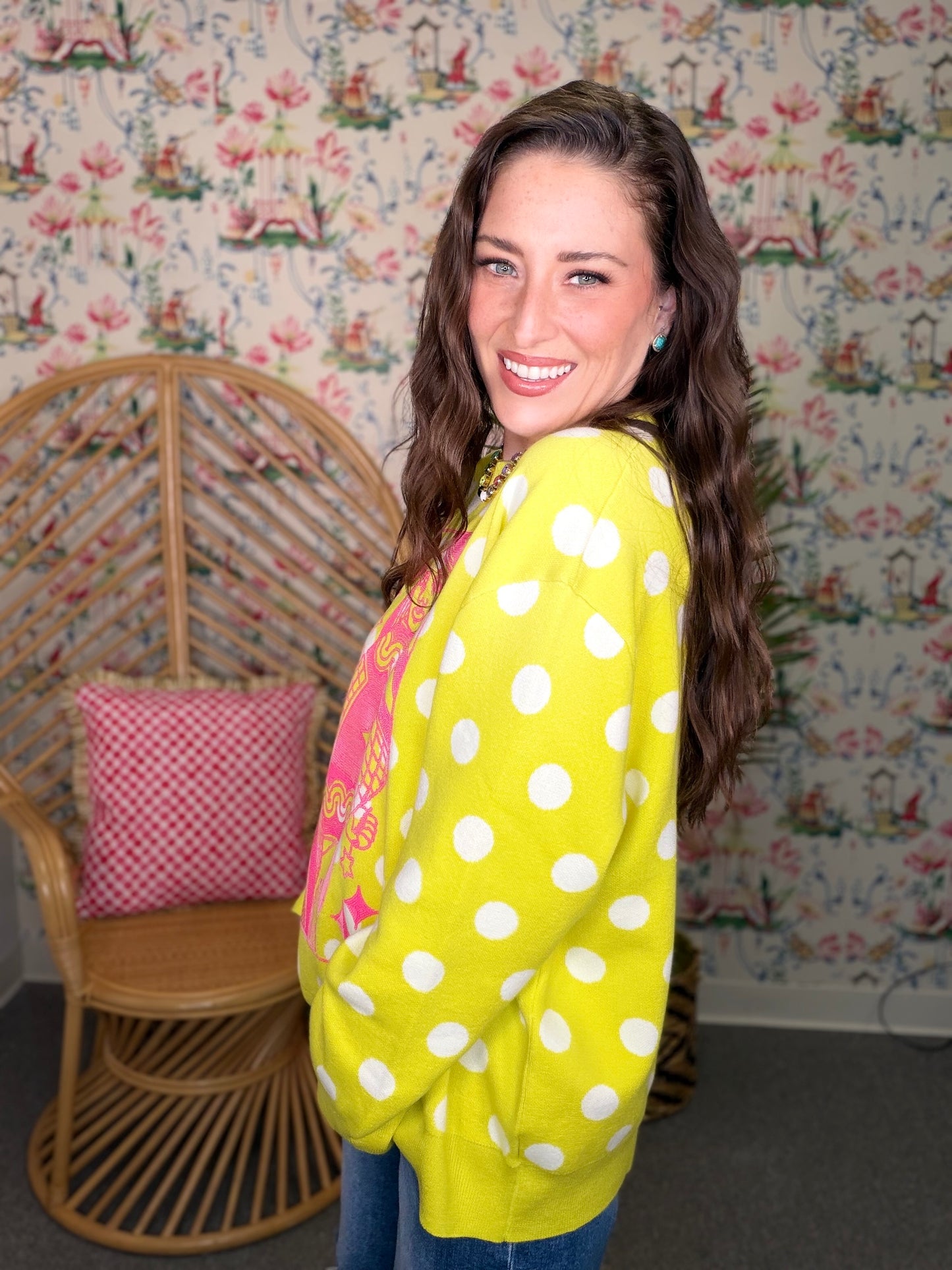 Woman wearing a bright yellow polka dot cardigan in a room with floral wallpaper.