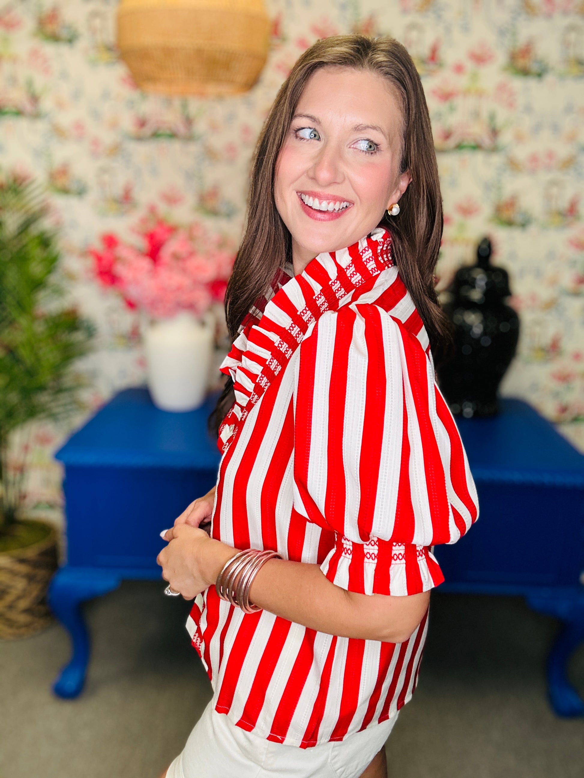 Woman wearing a red and white striped shirt in a room with floral wallpaper and blue furniture.