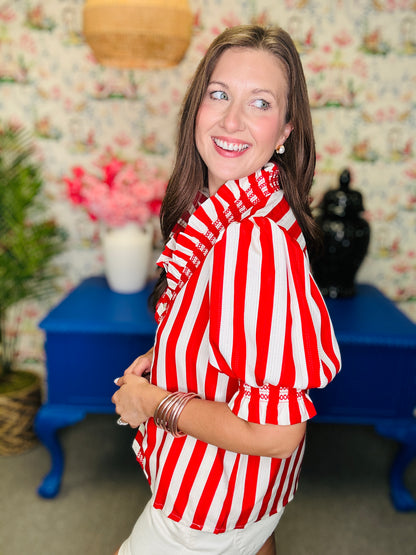 Woman wearing a red and white striped shirt in a room with floral wallpaper and blue furniture.