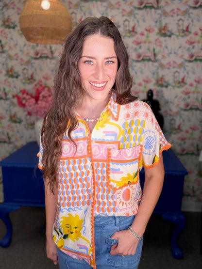 Woman wearing a colorful patterned shirt in a room with floral wallpaper.