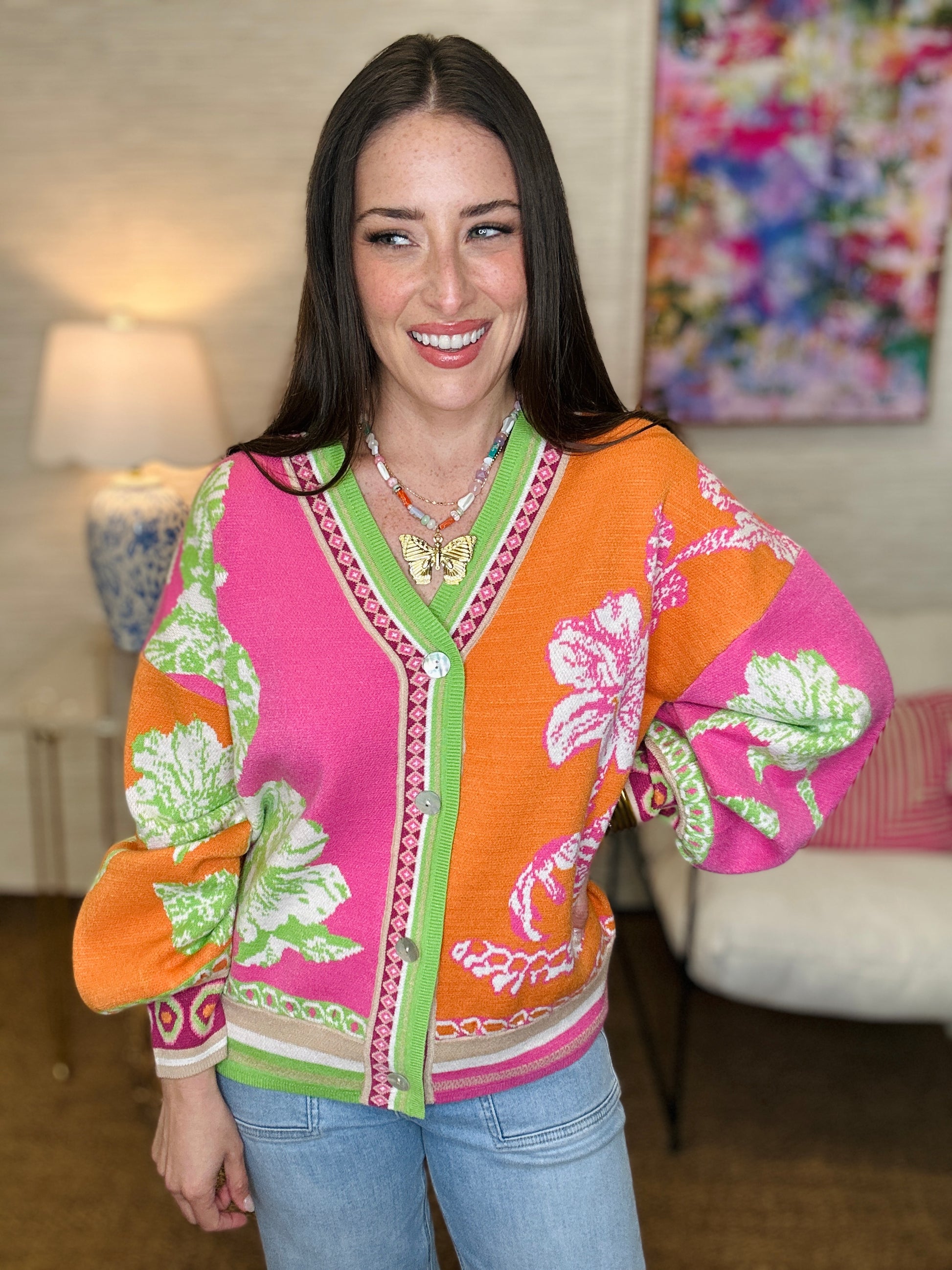 Woman wearing a colorful floral-patterned jacket in a room with a lamp and painting.