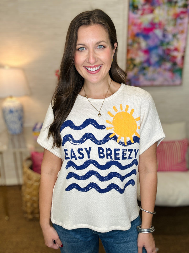 Woman wearing a white t-shirt with a sun and wave design and 'EASY BREEZY' text.