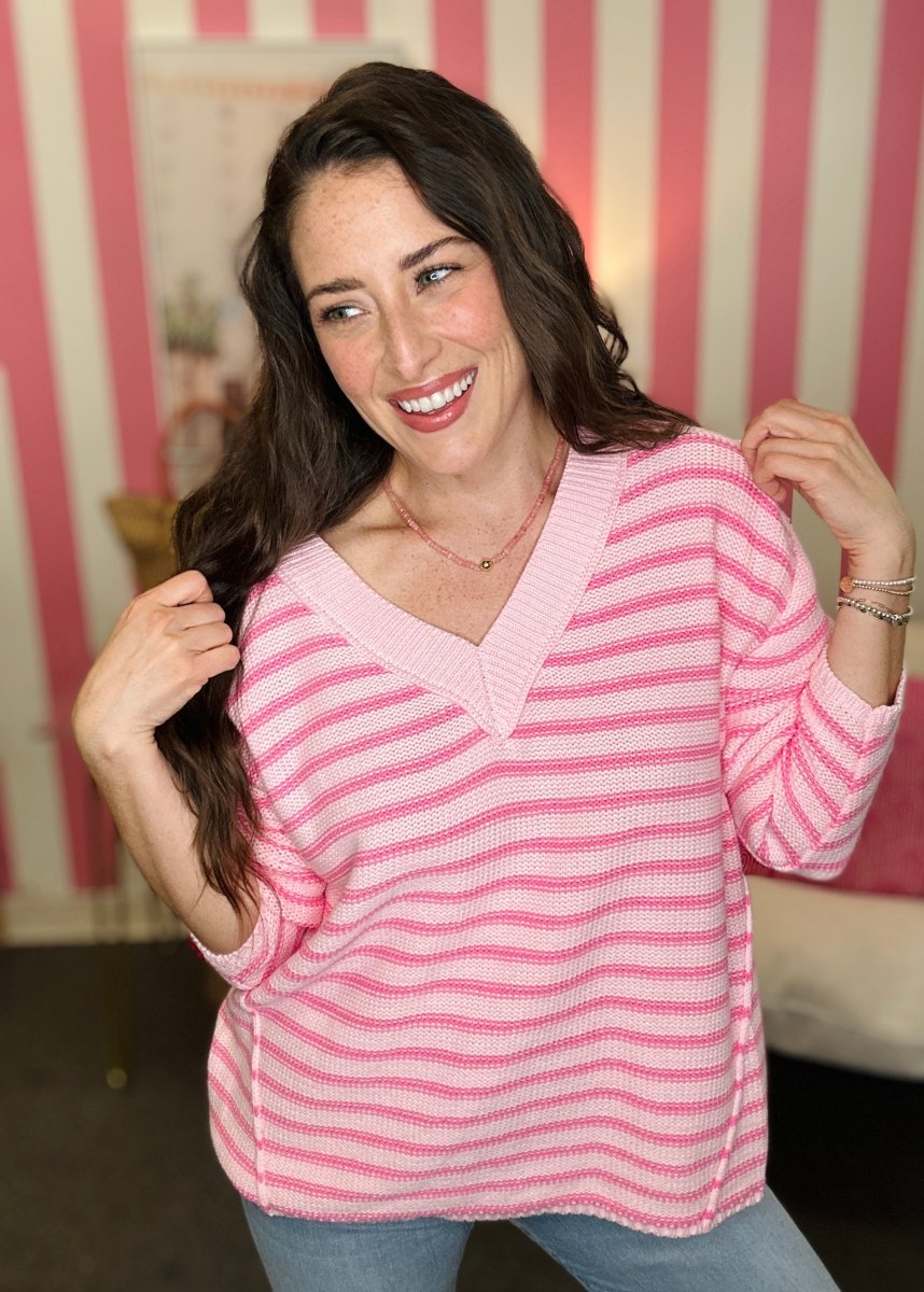 Woman wearing a pink striped sweater in front of a striped wall.