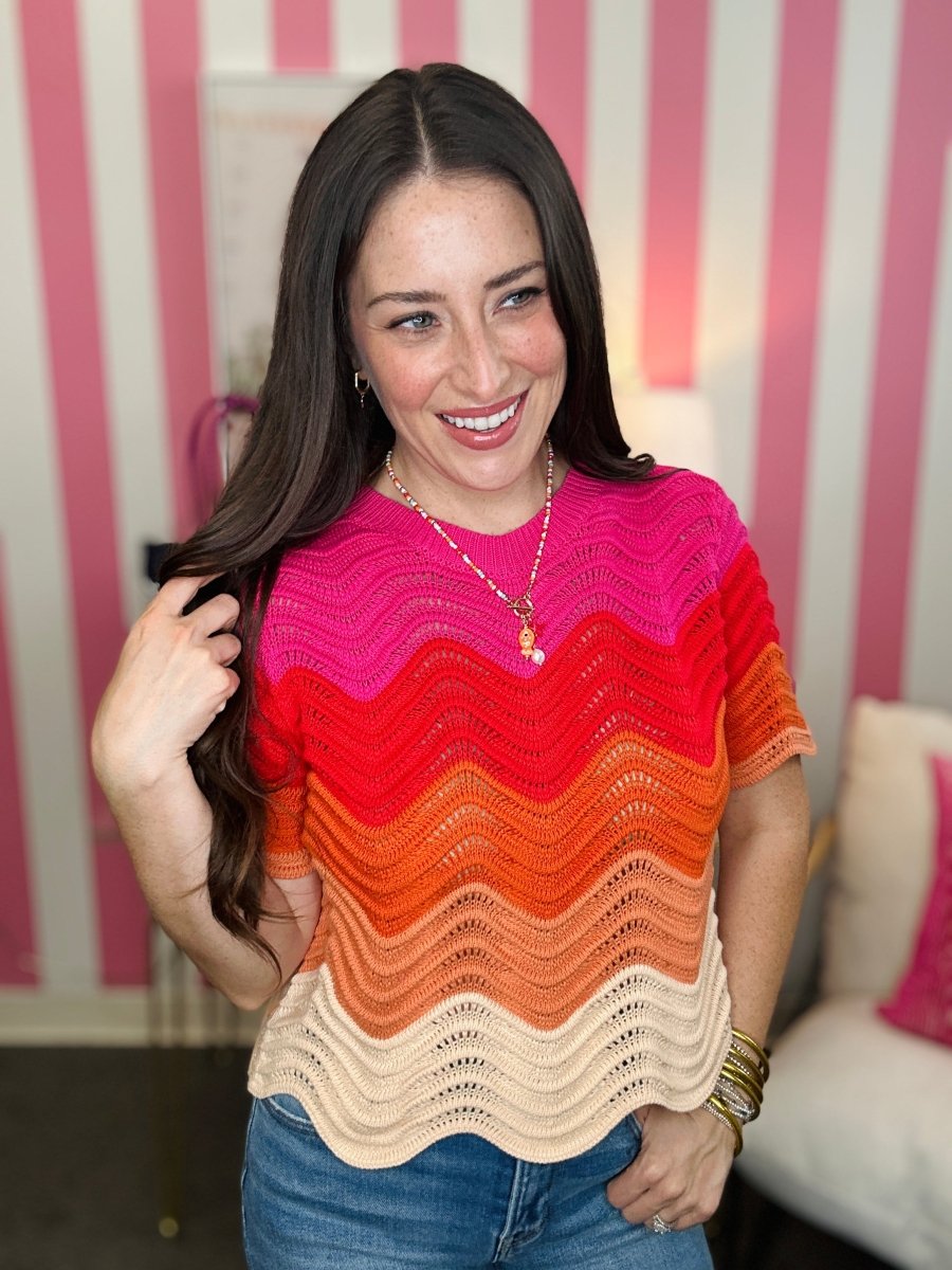 Woman wearing a colorful striped sweater in a room with pink and white striped walls.