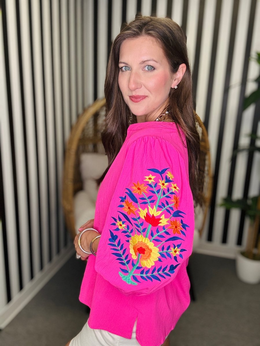 Woman wearing a bright pink top with colorful floral embroidery indoors.