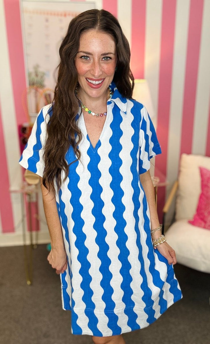 Woman wearing a blue and white striped dress in an indoor setting with pink and white striped walls.