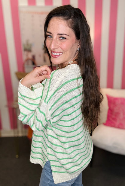 Woman wearing a white sweater with green stripes in a room with pink and white striped walls.