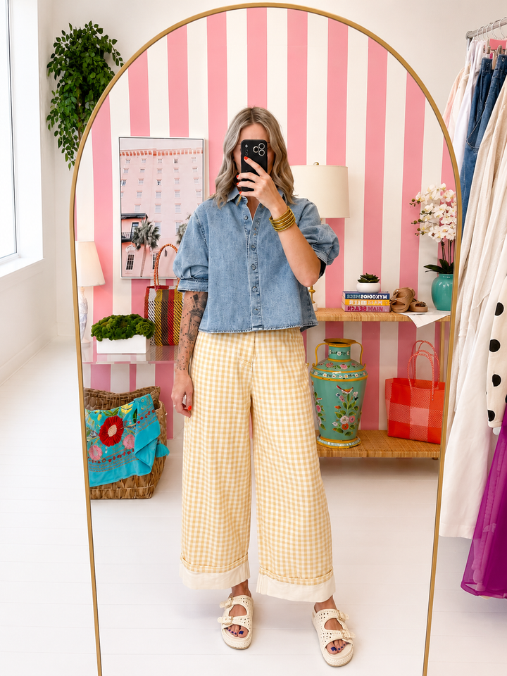 Person taking a mirror selfie wearing a denim shirt and yellow checkered pants in a room with striped walls.