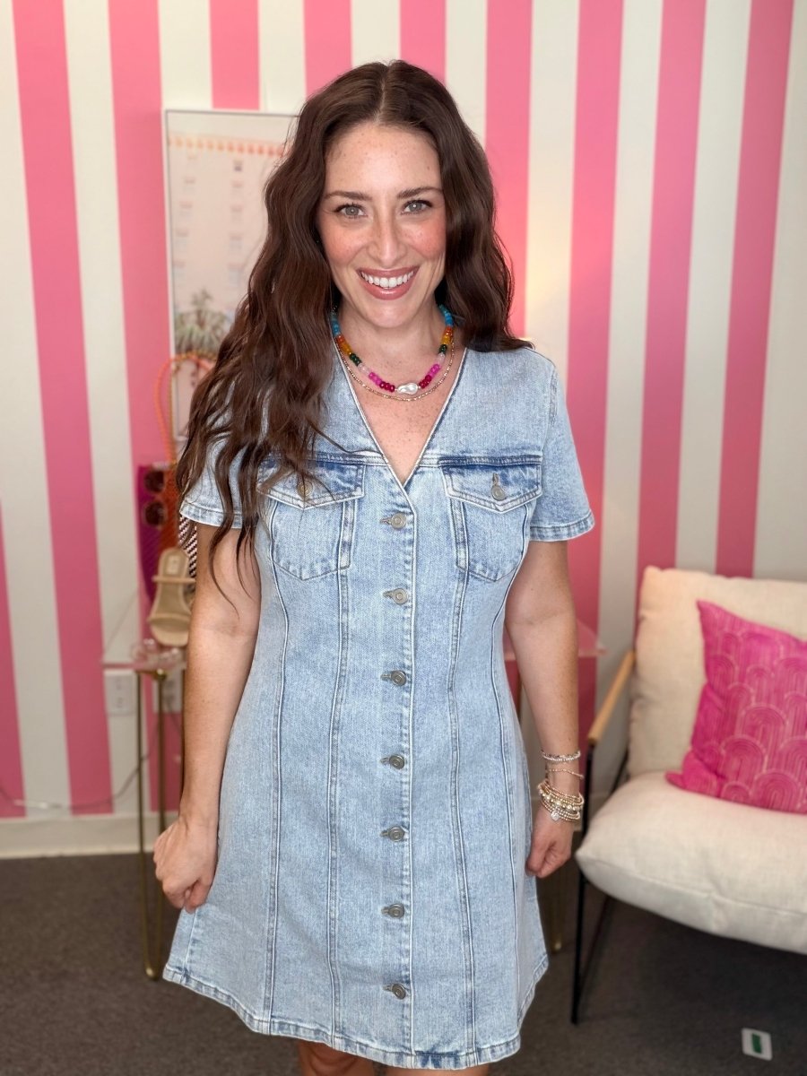 Woman wearing a denim dress in a room with pink and white striped walls.
