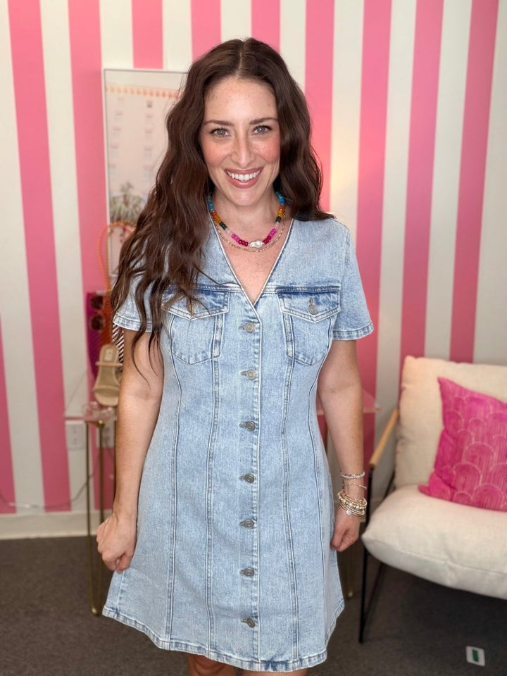 Woman wearing a denim dress in a room with pink and white striped walls.