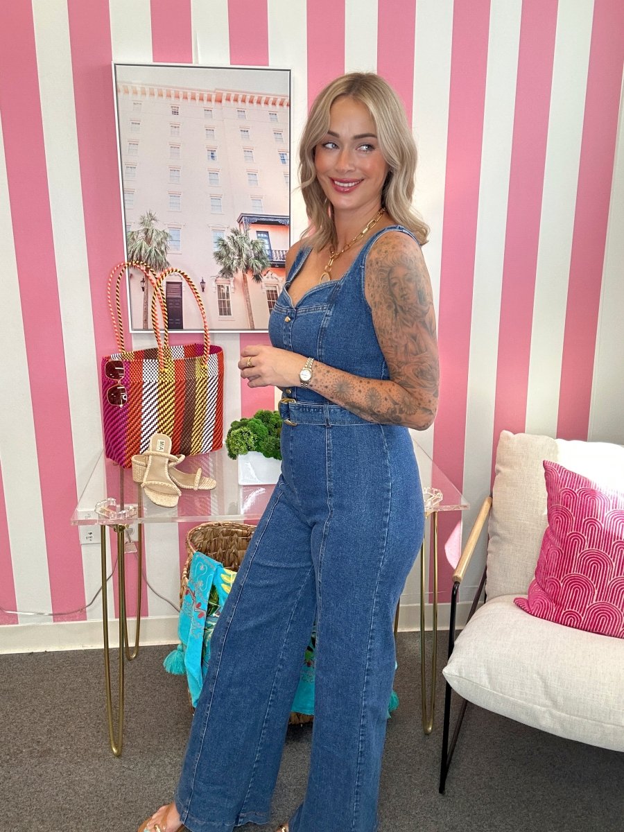 Woman in a blue denim jumpsuit standing in a room with pink and white striped walls.