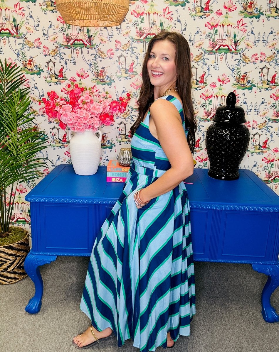 Woman in a striped dress standing in a room with colorful wallpaper and blue furniture.