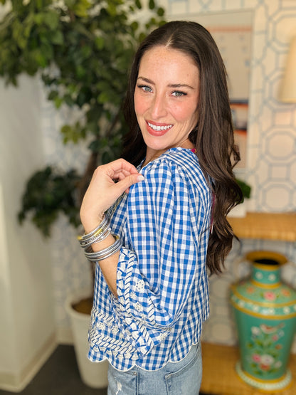 Woman wearing a blue and white checkered shirt in an indoor setting with plants and decor.