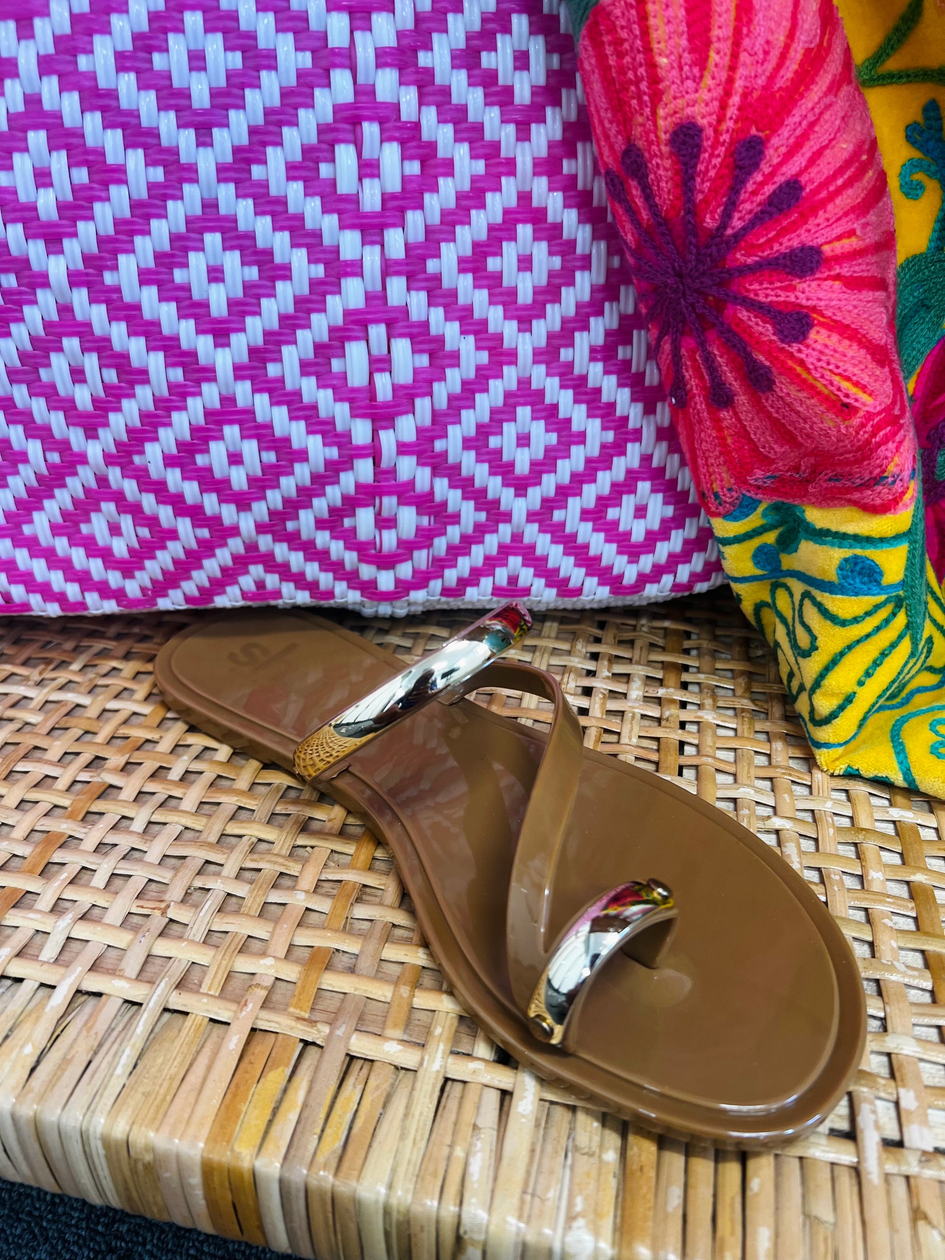 Brown sandal with gold toe ring on a woven surface with colorful fabric in the background