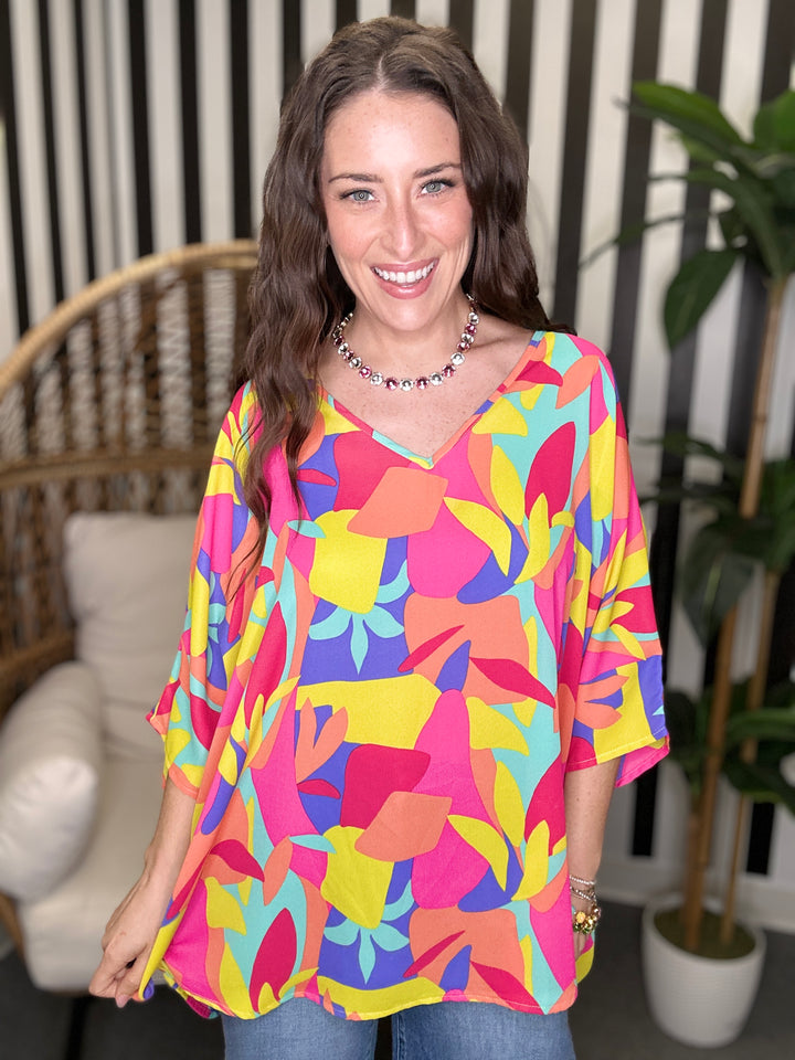 Woman wearing a colorful patterned top in an indoor setting with a plant and chair.