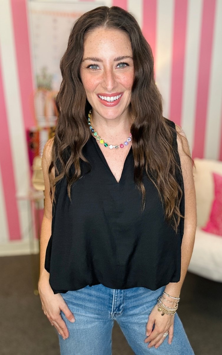 Woman wearing a black sleeveless top and blue jeans with a colorful necklace indoors.