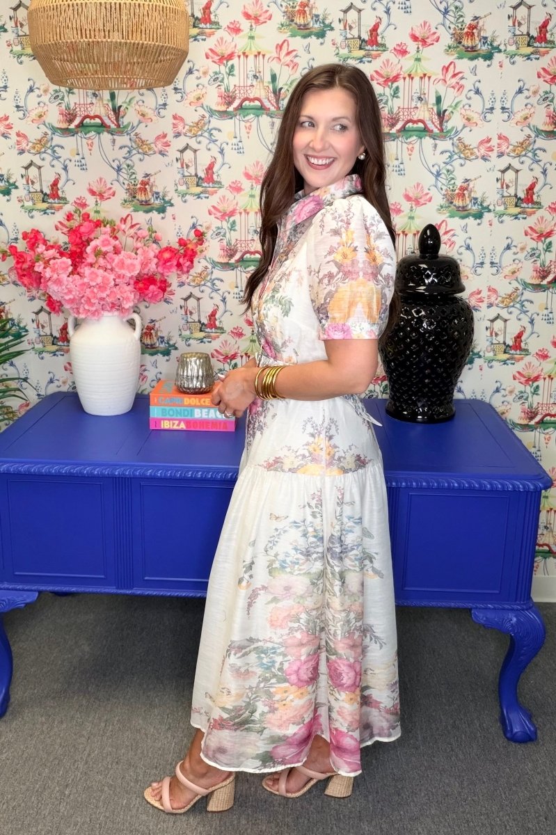 Woman in a floral dress standing in a room with colorful wallpaper and furniture.