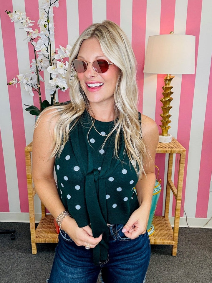 Woman wearing a green polka dot top in front of a pink and white striped wall.