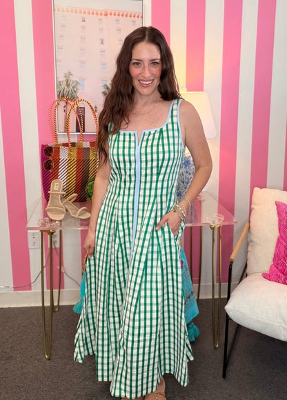 Woman in a green checkered dress standing in front of a pink and white striped wall.