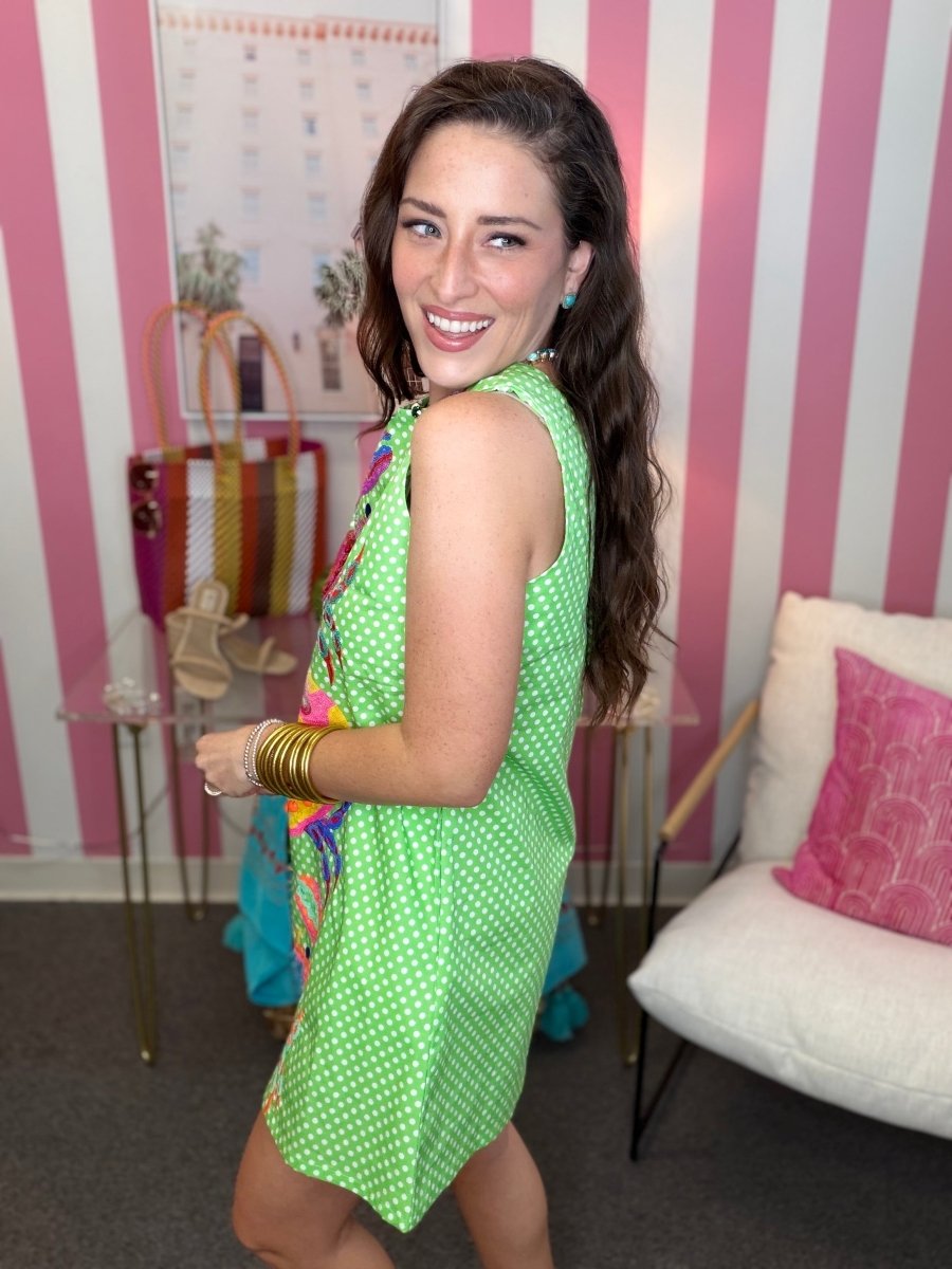 Woman in a green dress standing in a room with striped walls and a couch.