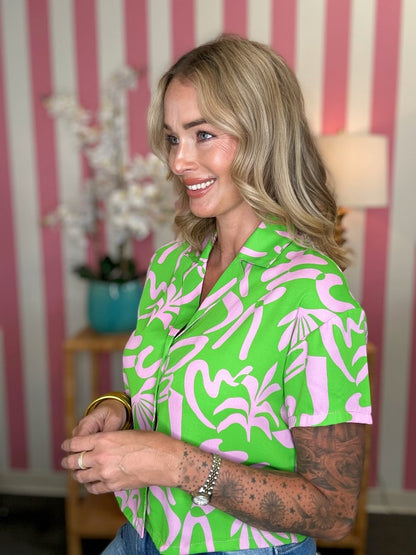 Woman wearing a green and pink patterned shirt in a room with striped wallpaper.