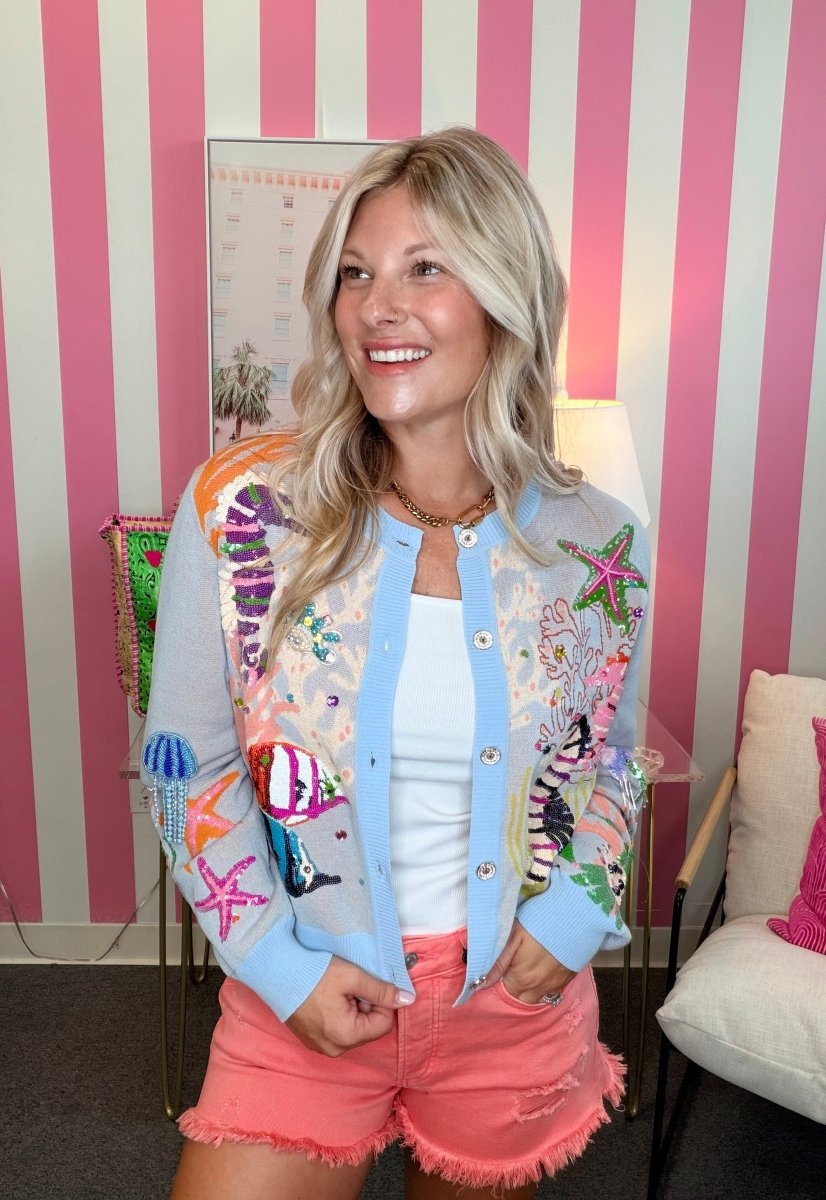 Woman wearing a colorful embroidered jacket and pink shorts in a room with striped walls.