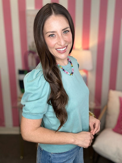 Woman wearing a light blue top with a colorful necklace in a room with striped walls.