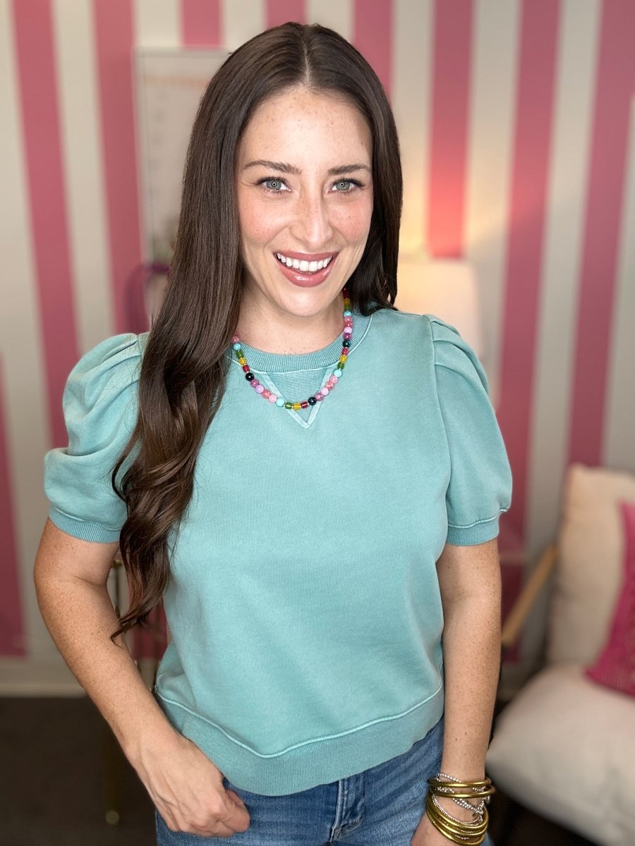 Woman wearing a light blue top with puffed sleeves in a room with striped walls.