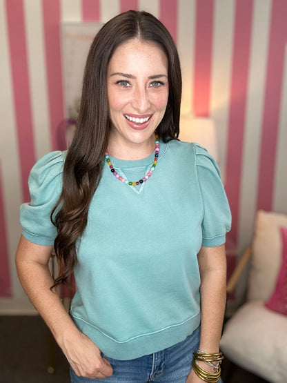Woman wearing a light blue top with puffed sleeves in a room with striped walls.