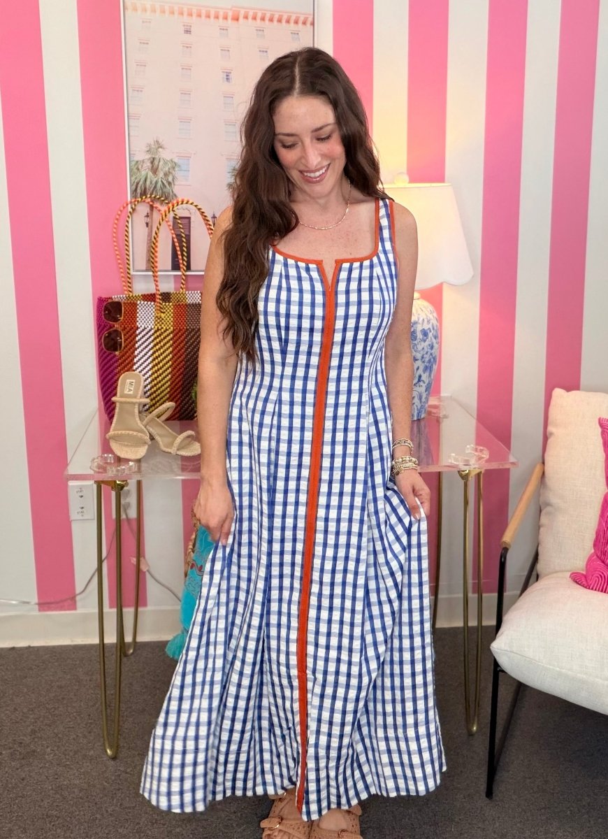 Woman wearing a blue and white checkered dress with orange accents in a room with pink and white striped walls.
