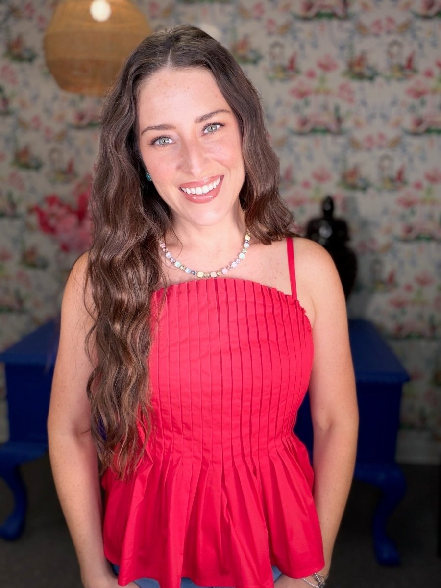 Woman wearing a red dress standing in a room with floral wallpaper.