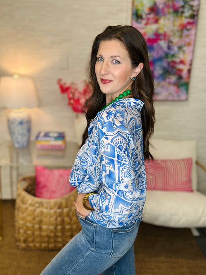Woman wearing a blue patterned blouse and jeans in a living room setting.