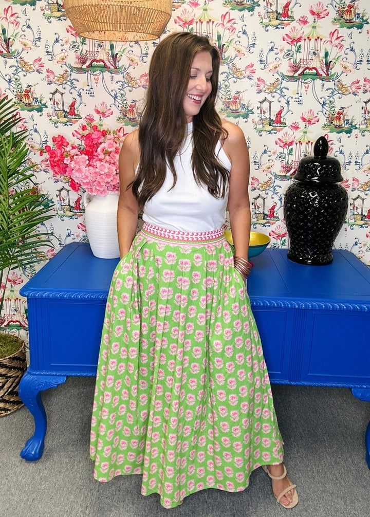 Woman in a white top and green floral skirt standing in front of a colorful patterned wall.
