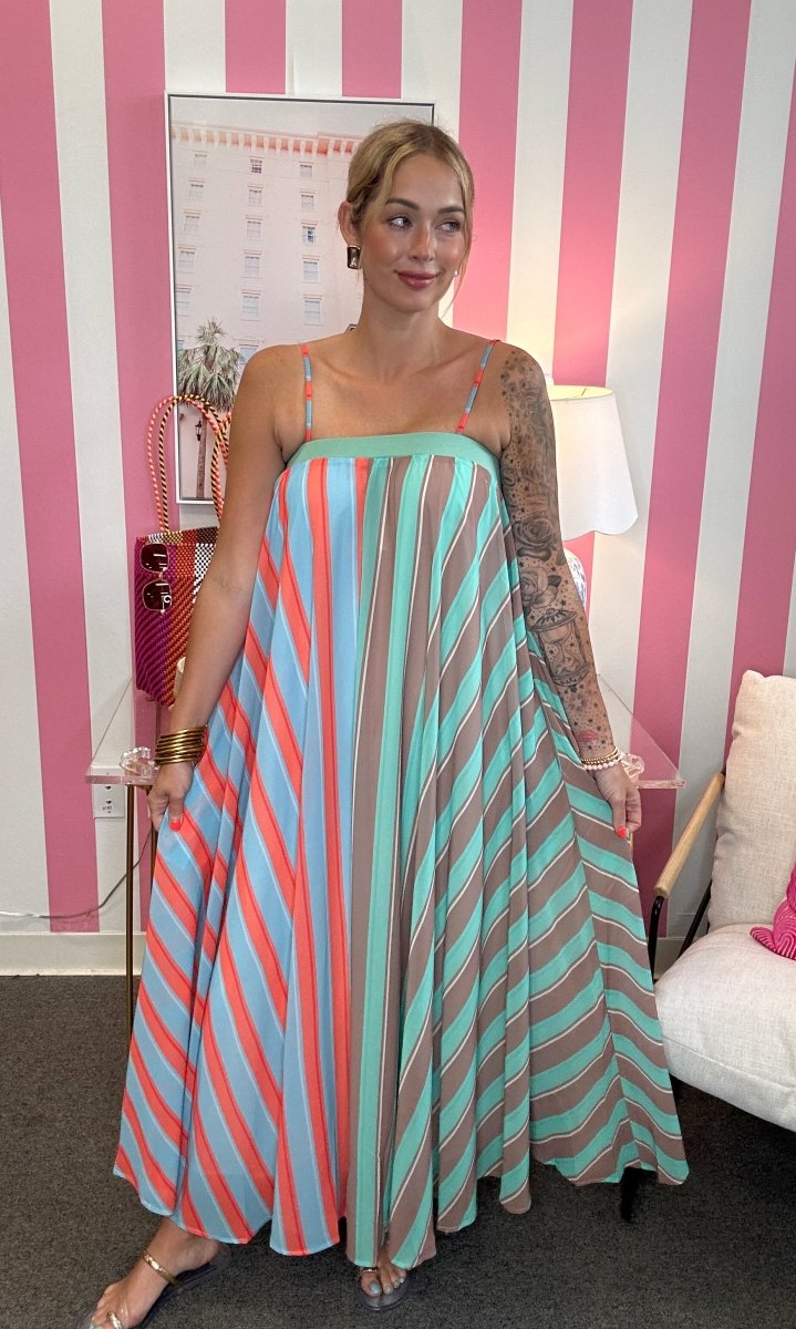Woman wearing a colorful striped dress in a room with pink and white striped walls.