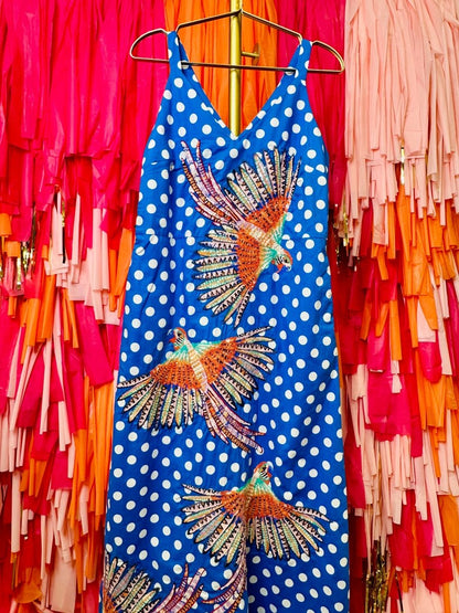 Blue dress with white polka dots and colorful bird designs on a hanger against a colorful background.