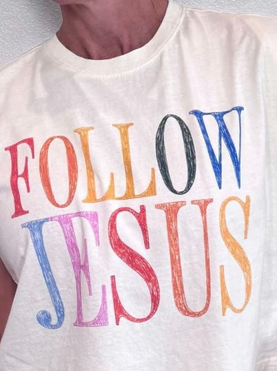 A close-up of a person wearing a white crew-neck t-shirt with the words 'FOLLOW JESUS' printed across the chest in large, colorful, textured letters.