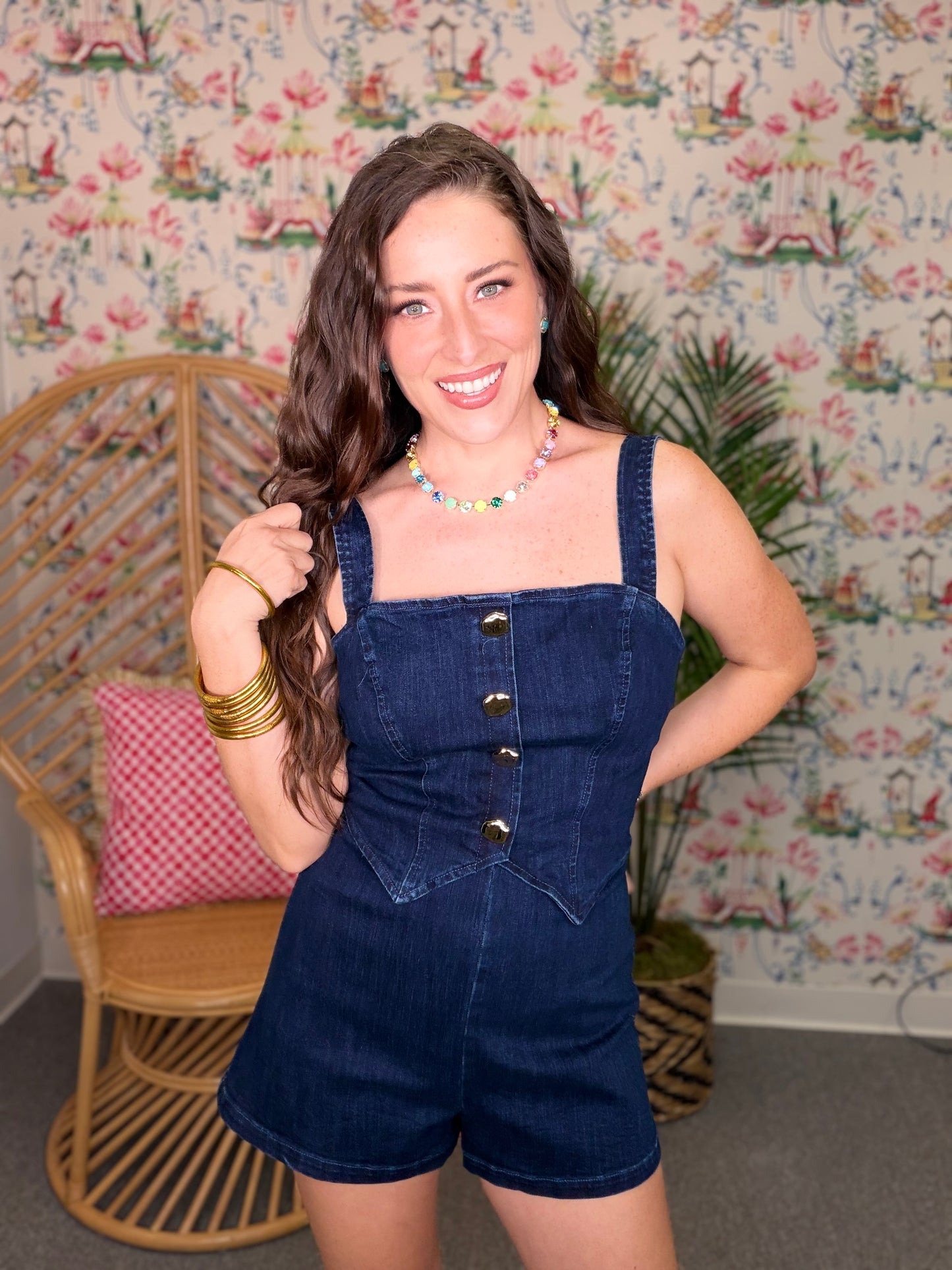Woman wearing a denim romper standing in front of a patterned wall.