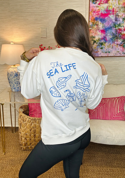 Person wearing a white sweatshirt with 'The Sea Life' design in a living room.