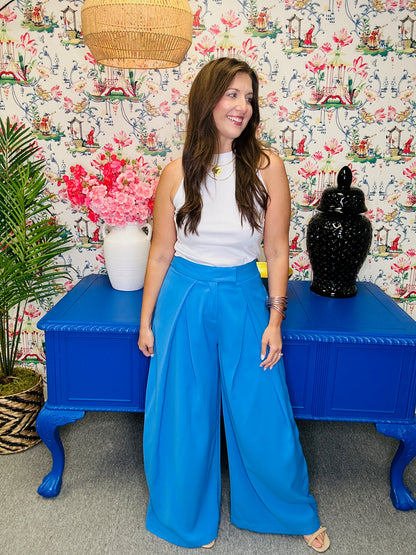 Woman in blue pants and white top standing in front of a colorful wall with floral patterns.